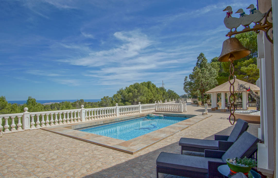 Outdoor terrace with a mosaic-tiled pool and white balustrade, overlooking the Mediterranean coastline and lush pine forests.