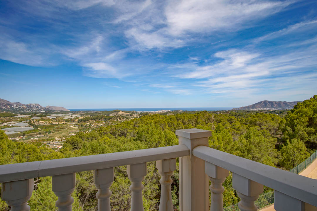 Panoramic view from the terrace with a classic white balustrade, overlooking the Mediterranean Sea and the dense pine forests of the Costa Blanca.