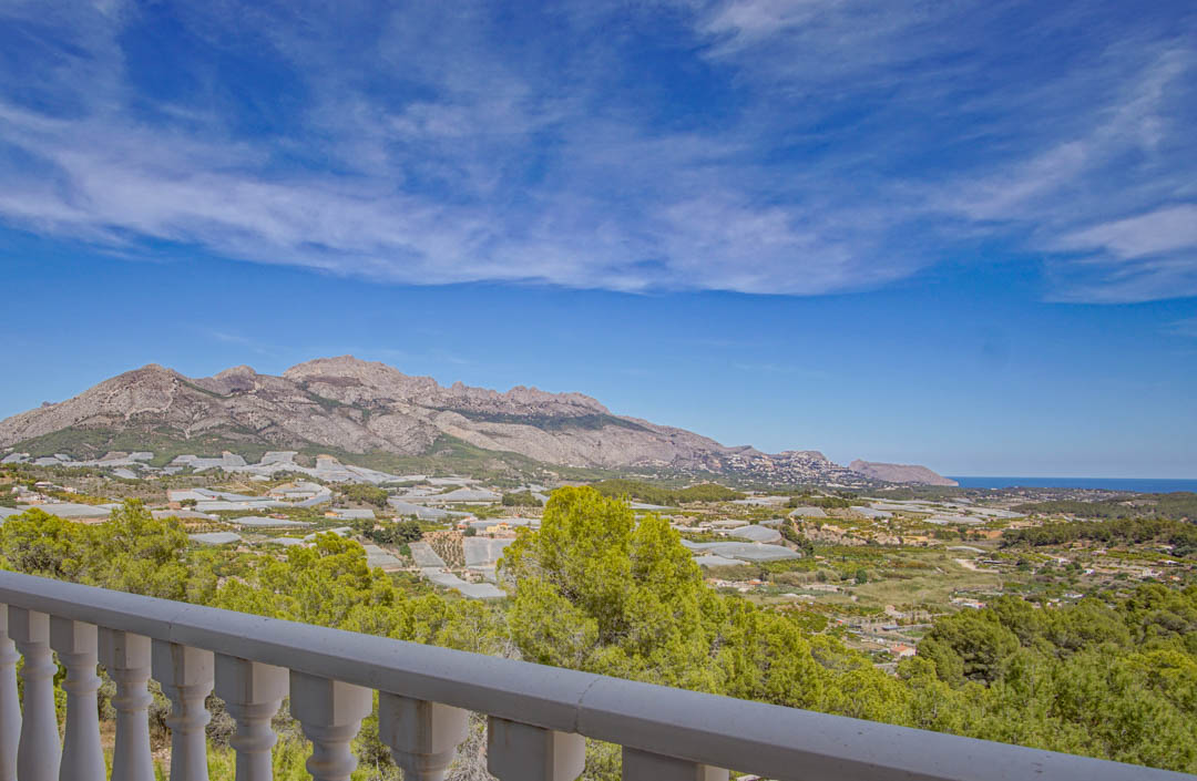 Panoramic views from the terrace with a white stone balustrade, overlooking the Mediterranean valley, rugged mountains, and the sea horizon.
