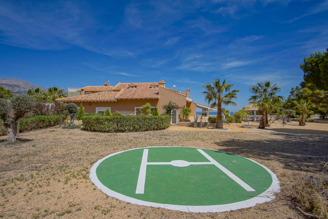 Private helipad situated within the expansive grounds, featuring a circular landing pad adjacent to the Mediterranean villa and landscaped gardens with palm trees.