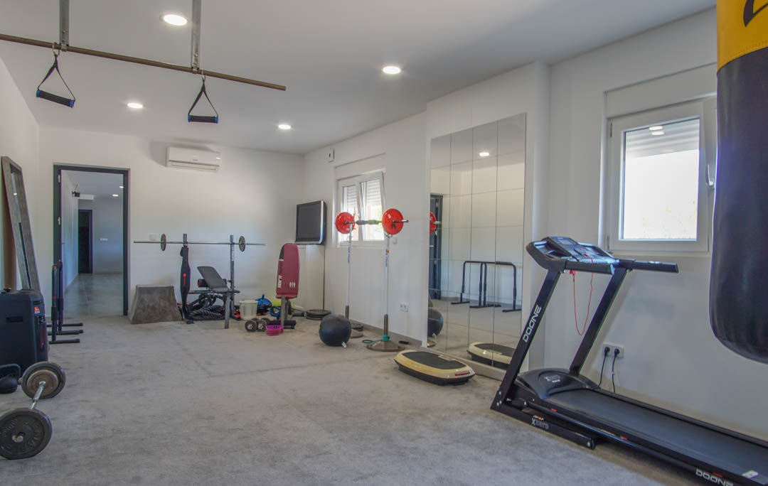 Private home gym featuring a treadmill, punching bag, and weight station. The space includes recessed lighting, wall mirrors, and split-system air conditioning.