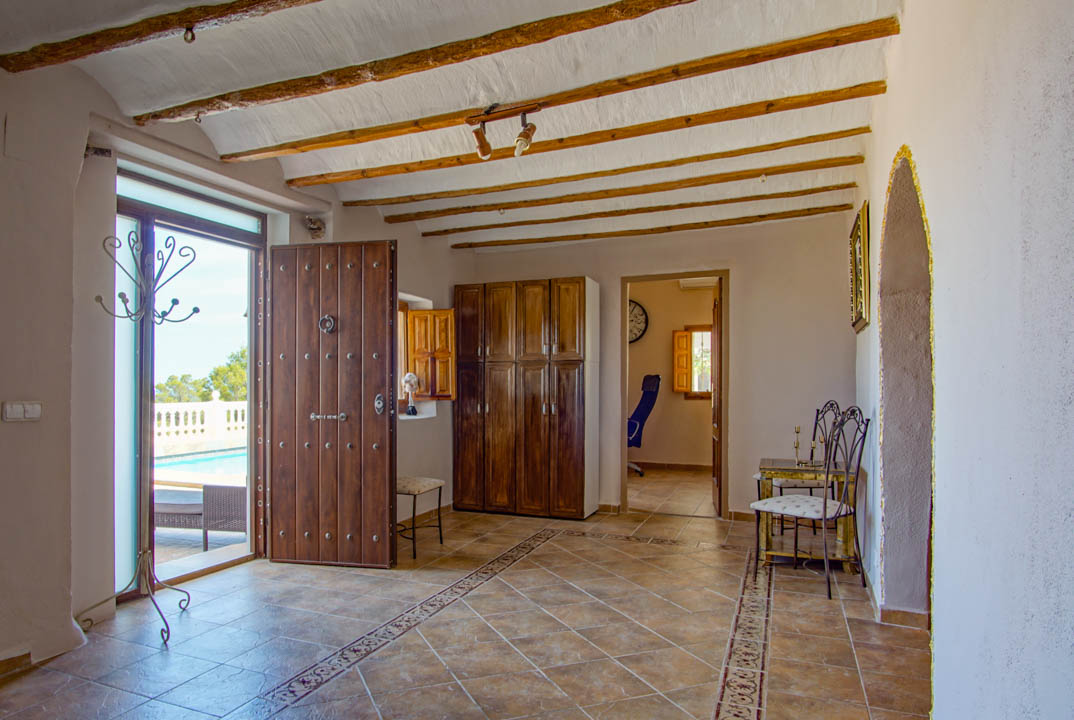 Rustic entrance hall featuring exposed wooden ceiling beams, decorative tiled flooring, and a solid wood studded door opening onto the outdoor pool terrace.