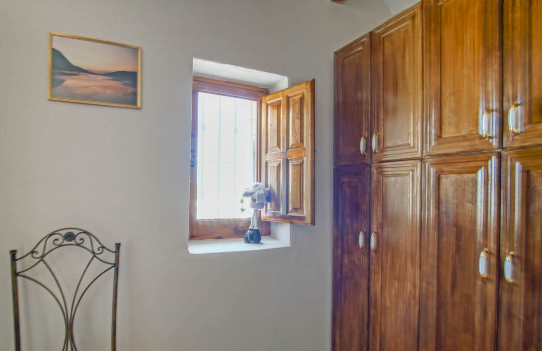 Rustic room featuring a solid wood built-in wardrobe, a traditional window with wooden shutters, and a decorative wrought iron chair.