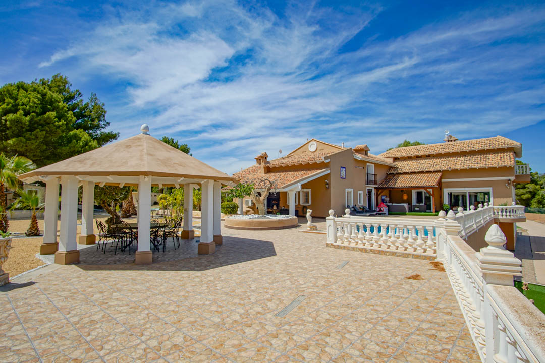 Spacious outdoor terrace featuring stone tiling, a classic white balustrade, and an octagonal gazebo with a dining area overlooking the main villa.