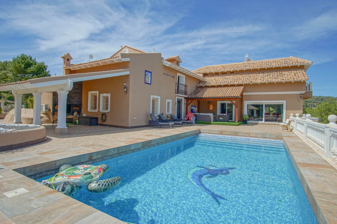 Swimming pool featuring a decorative mosaic, surrounded by a spacious stone terrace and a covered outdoor lounge area with a rustic fireplace and white columns.
