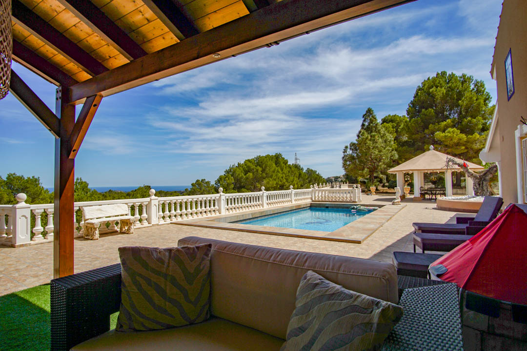 Terrace with swimming pool, white balustrade, and panoramic sea views. Includes a wooden pergola lounge area and a separate pavilion among Mediterranean pines.