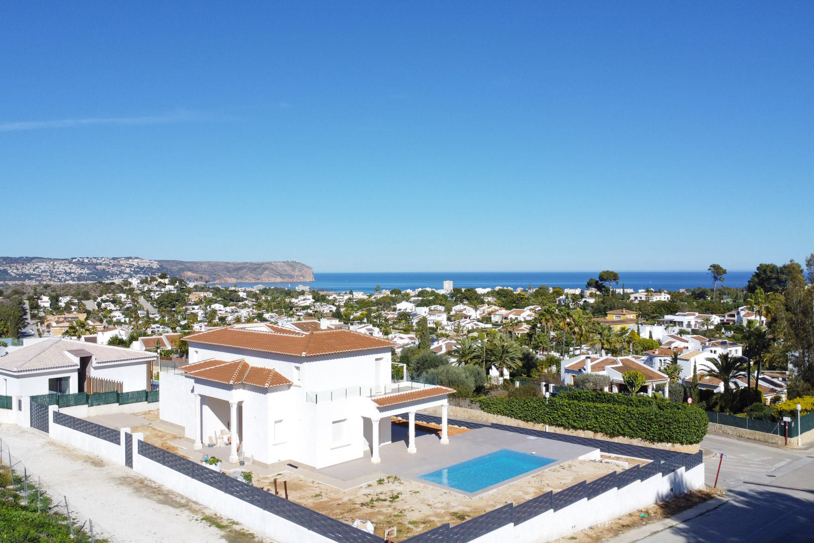 Aerial view of the villa in Pinosol featuring a terracotta roof, rectangular pool, and panoramic views of the Mediterranean Sea and Jávea coastline.