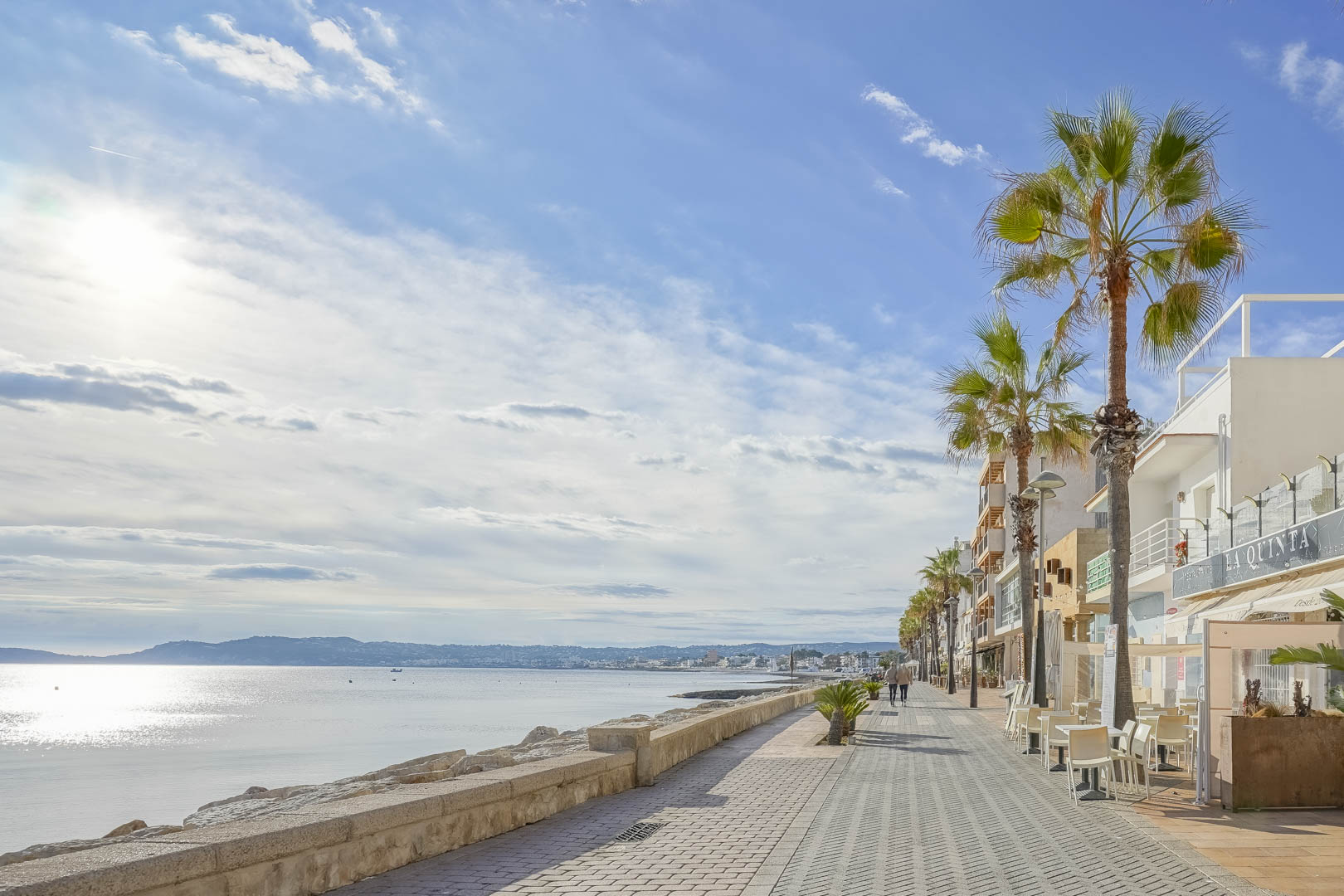 Coastal promenade in Jávea featuring a paved walkway, palm trees, and Mediterranean sea views, located just five minutes from the villa.