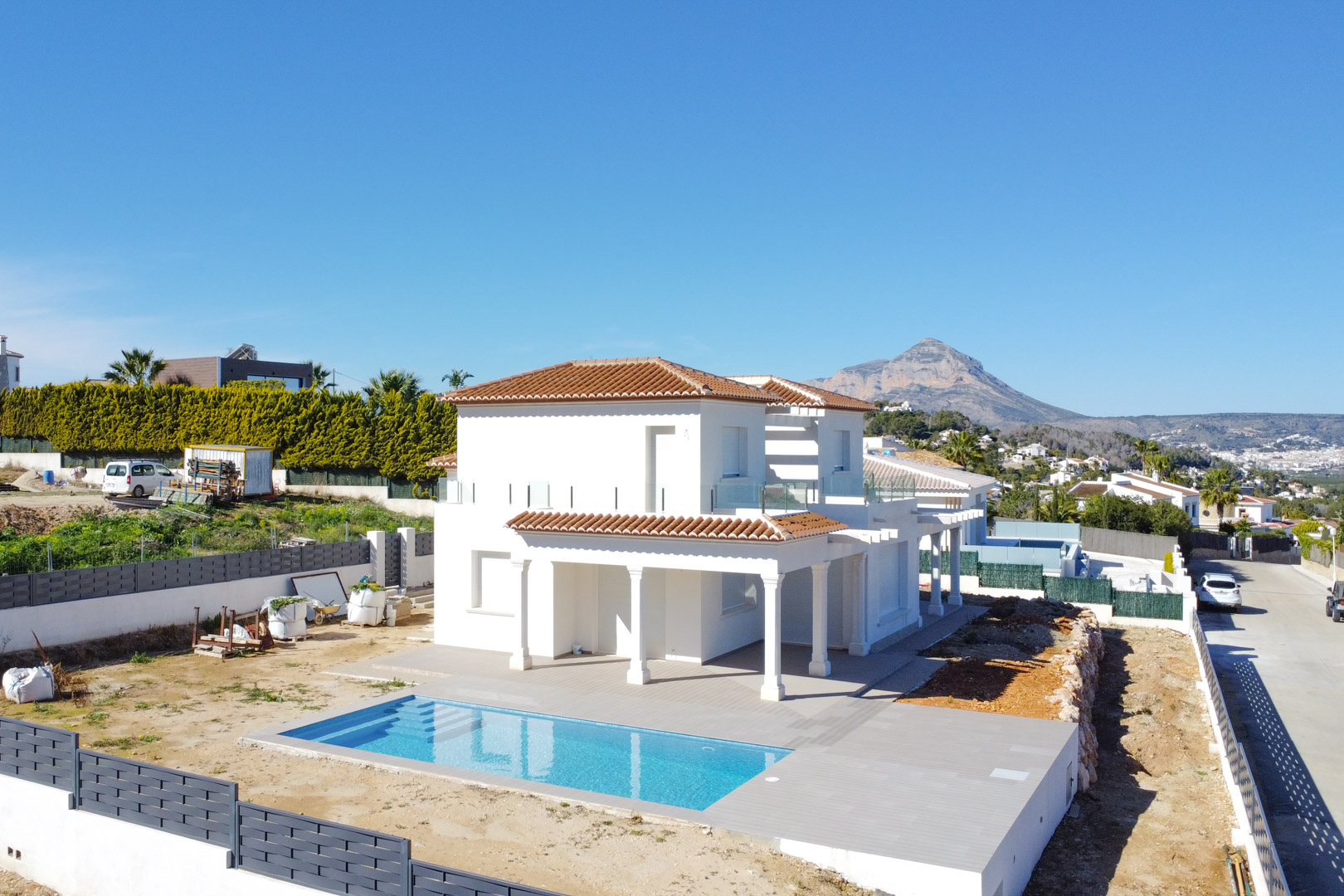 Elevated exterior view of the villa featuring a rectangular swimming pool, spacious tiled terrace, and the iconic Montgó mountain in the distance.