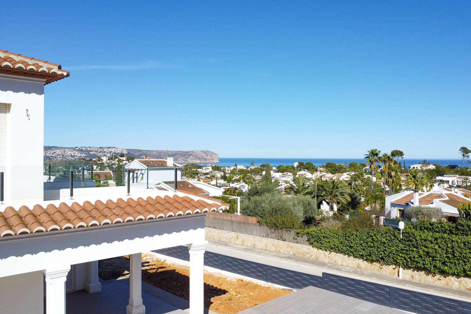 Elevated view from the upper terrace featuring glass balustrades, traditional terracotta roofing, and panoramic vistas of the Mediterranean Sea and coastline.