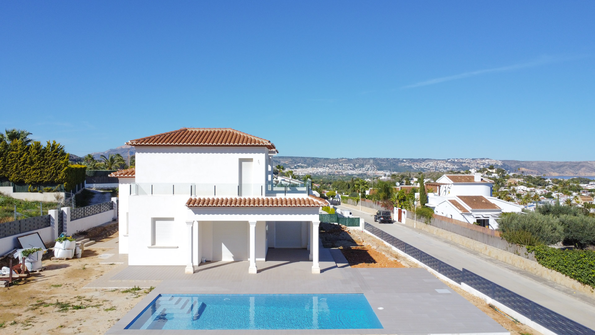 Exterior view of the villa showing the rectangular swimming pool, white two-story facade, and upper terraces with glass balustrades against a clear sky.