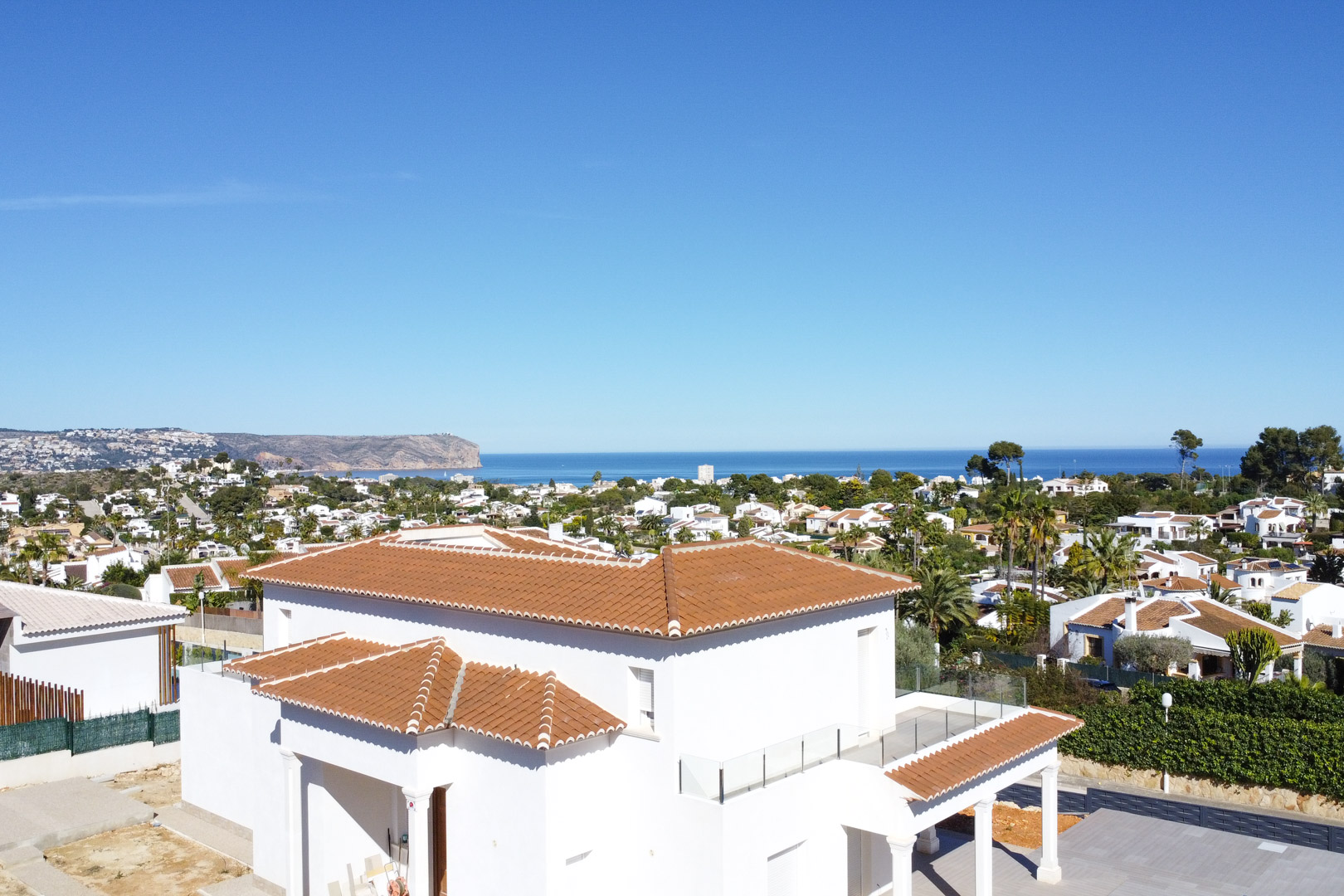 View of the villa's white exterior and terracotta roof, featuring upper terraces with glass balustrades and panoramic vistas of the Mediterranean Sea.