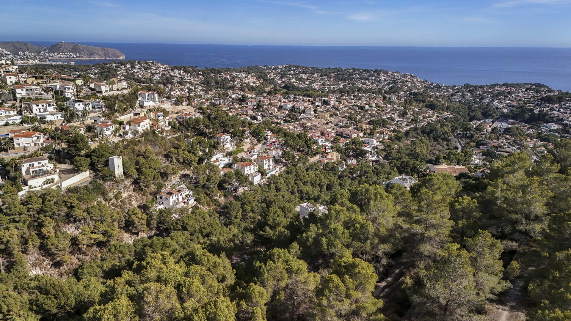 Aerial view showcasing the residential integration within Benissa's natural landscape, featuring dense pine forests and panoramic views of the Mediterranean Sea.