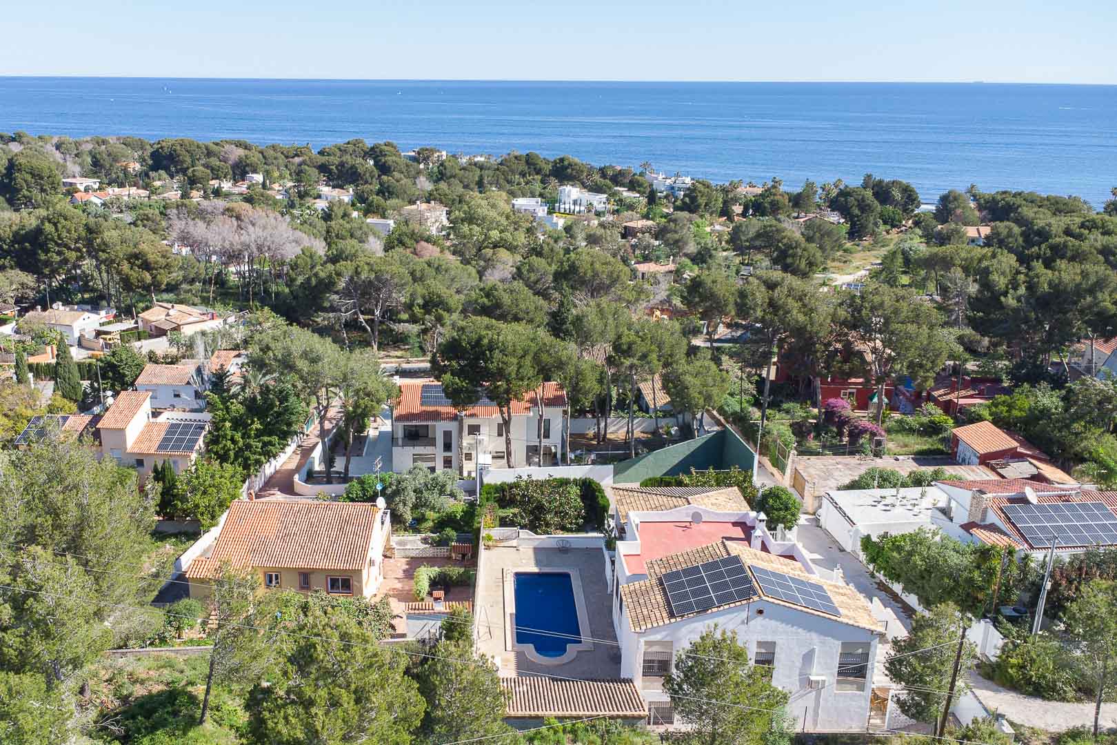 Aerial view of the villa in Las Rotas, featuring a private pool, solar panels, and a lush Mediterranean pine setting with sea views.