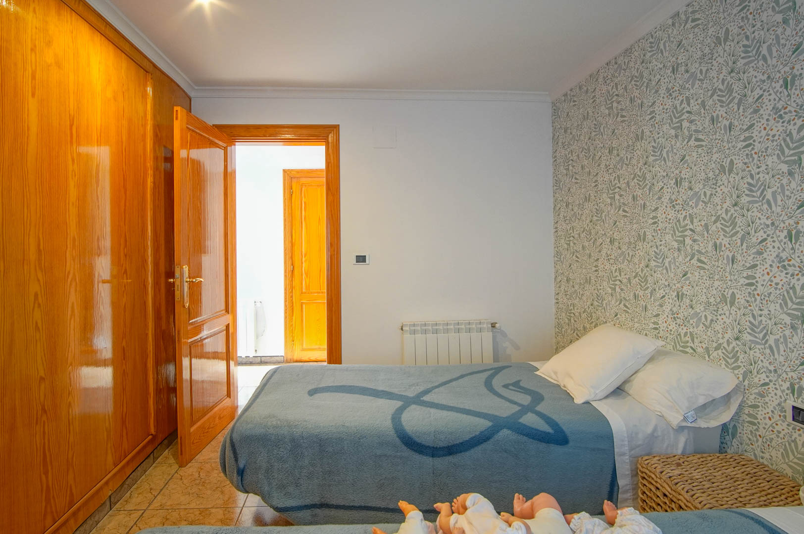 Bedroom featuring a polished wood built-in wardrobe, botanical print wallpaper, ceramic tile flooring, and a wall-mounted radiator.