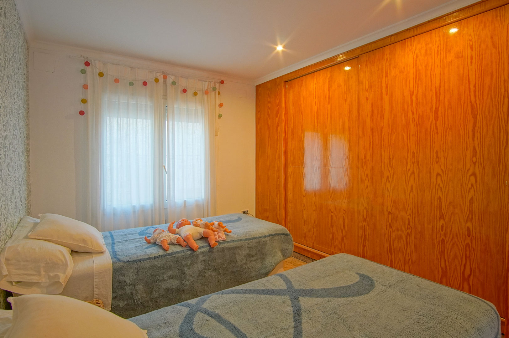 Bright bedroom featuring twin beds, floral patterned wallpaper, and a large built-in wooden wardrobe with a glossy natural finish.