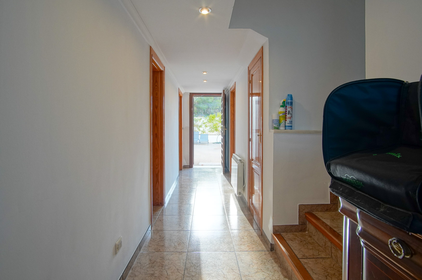 Bright hallway featuring ceramic tile flooring, wooden door frames, and recessed lighting, leading directly to an outdoor terrace area.