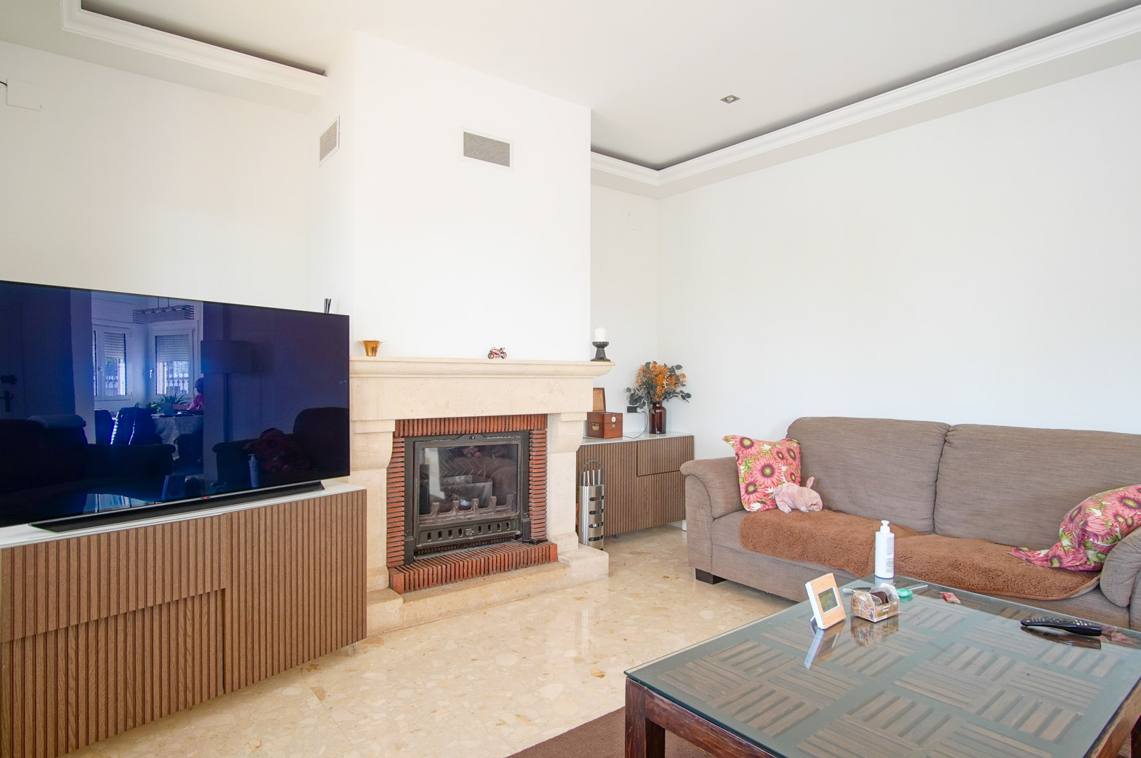 Bright living area featuring a stone fireplace with brick detailing, polished marble flooring, and custom wood cabinetry housing the media center.