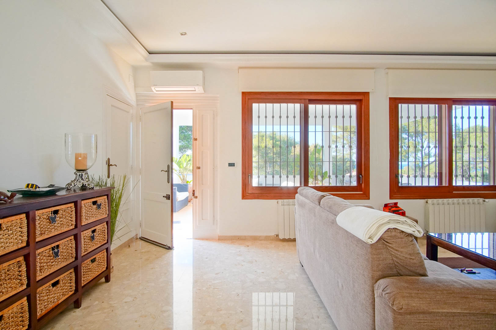 Bright living area featuring polished marble floors, wooden window frames, and terrace access. Includes split air conditioning and radiators for year-round comfort.