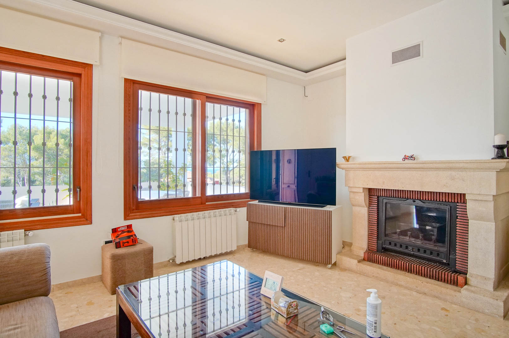 Bright living room featuring a carved stone fireplace, marble flooring, and large wooden windows overlooking the Mediterranean pine forest.