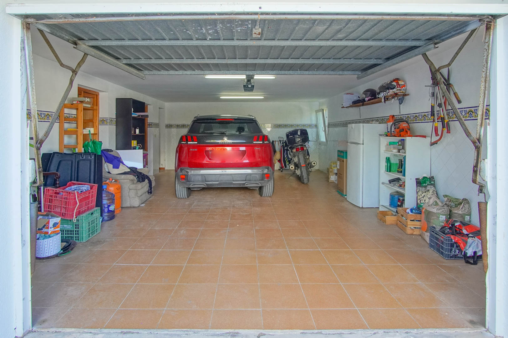 Enclosed garage in the semi-basement featuring ceramic tile flooring, fluorescent lighting, and ample space for vehicles and organized storage.