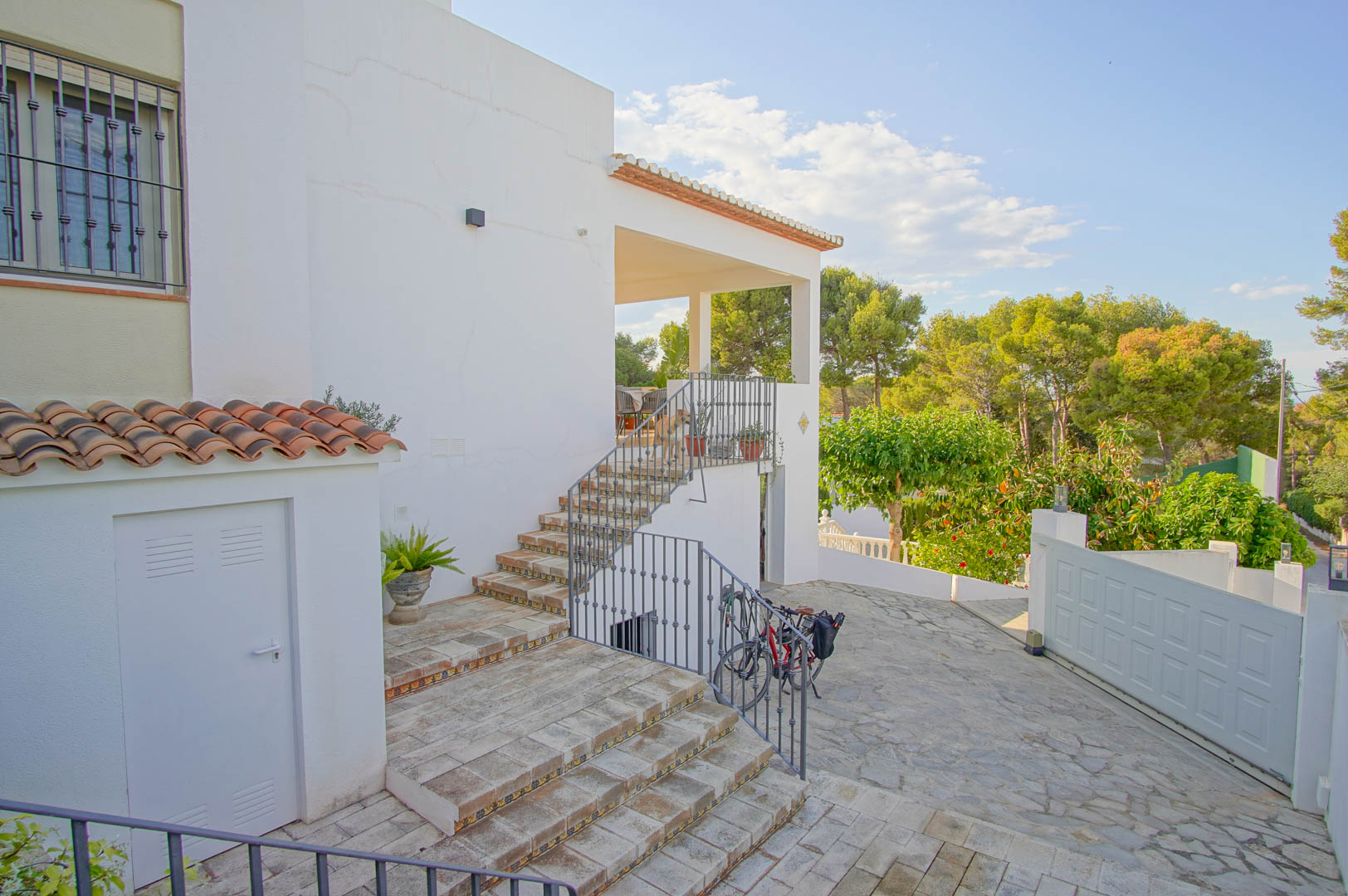 Exterior entrance featuring tiled stairs with decorative risers leading to a covered terrace, set against a backdrop of lush Mediterranean pines.
