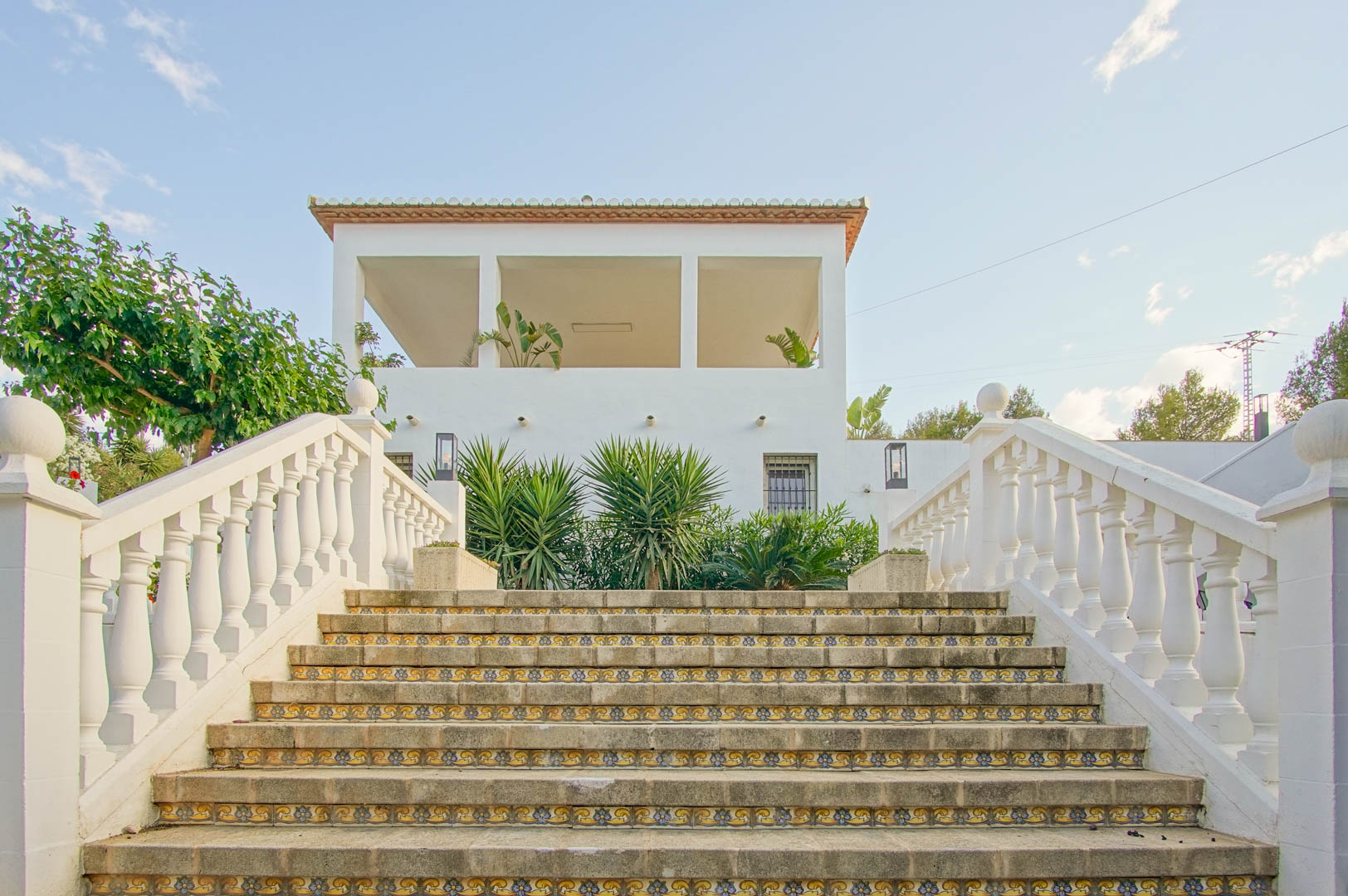 Exterior stone staircase featuring decorative ceramic tile risers and a white balustrade, leading toward the upper terrace and Mediterranean facade.