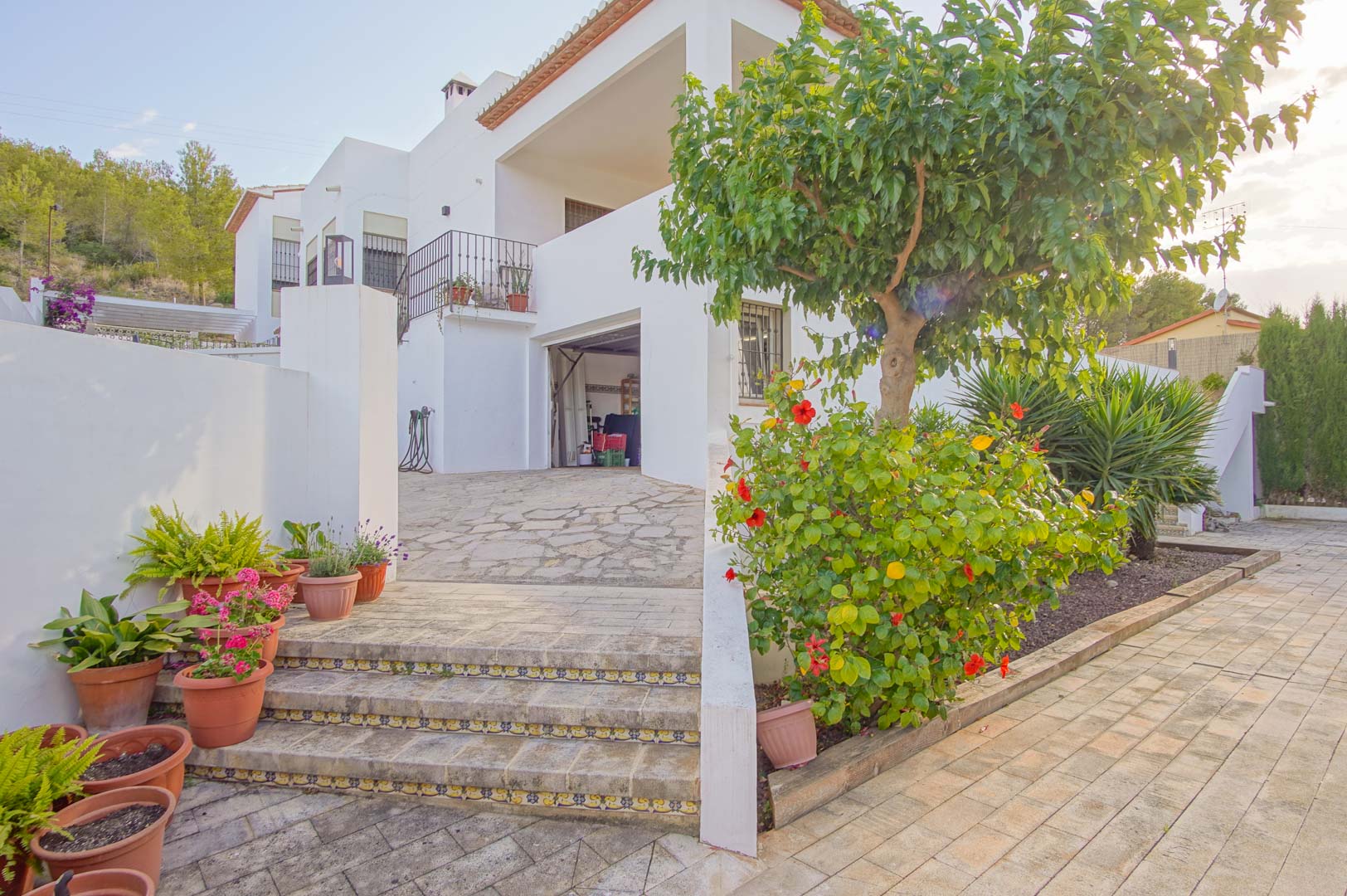 Exterior view of the garage entrance and lower level, featuring stone steps with decorative tile accents and vibrant Mediterranean landscaping.