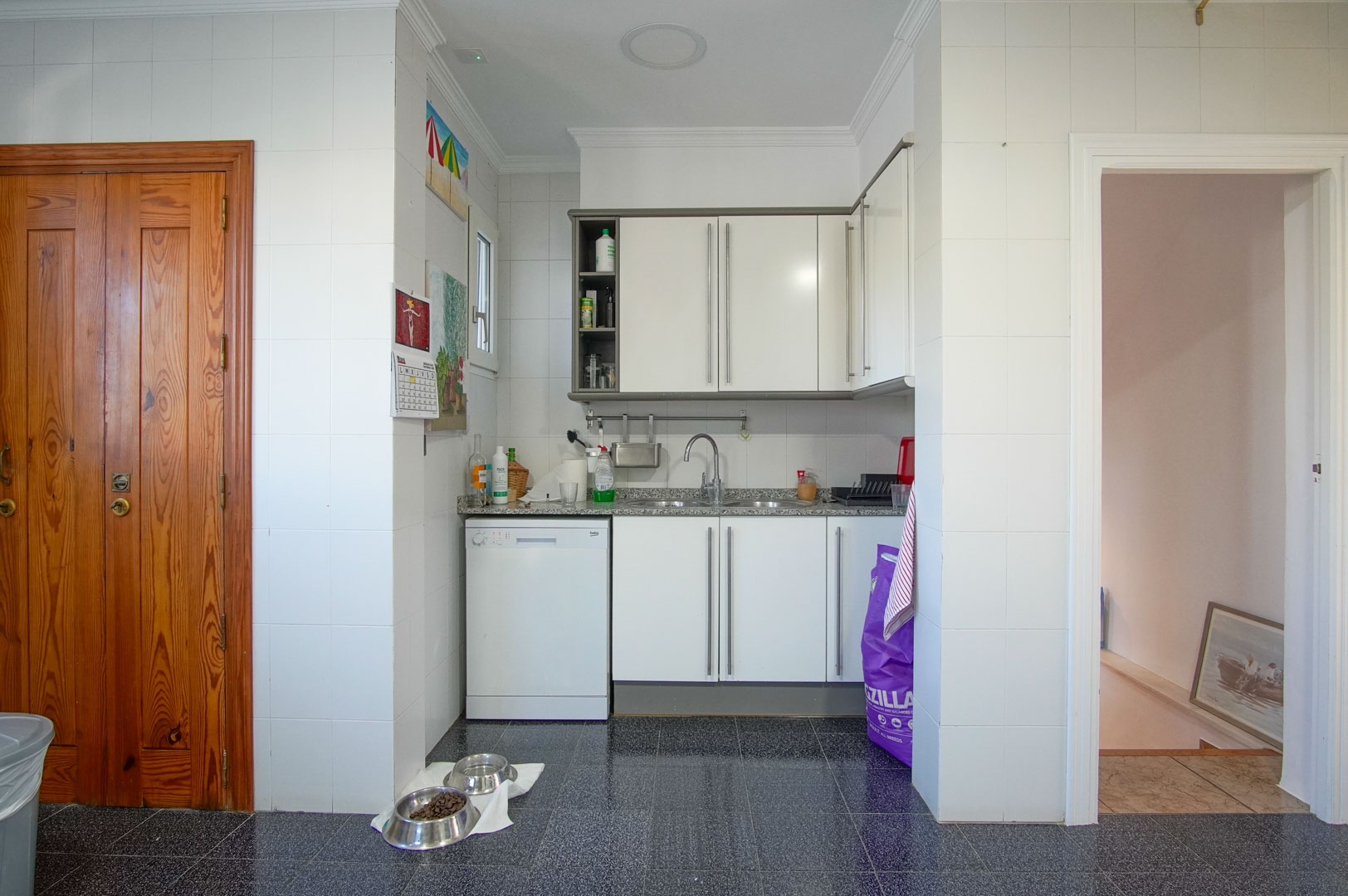 Functional guest apartment kitchen featuring white cabinetry, granite countertops, and dark terrazzo flooring, located adjacent to the internal staircase access.