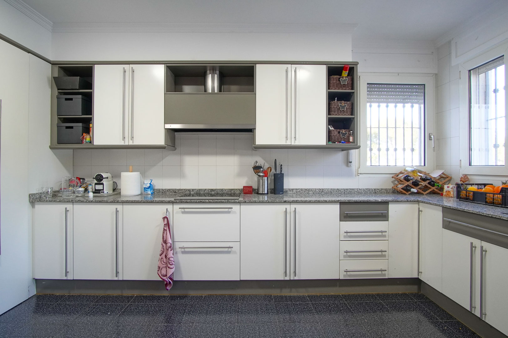Independent kitchen featuring white cabinetry, grey granite countertops, and an integrated induction hob. Natural light enters through windows with security bars.