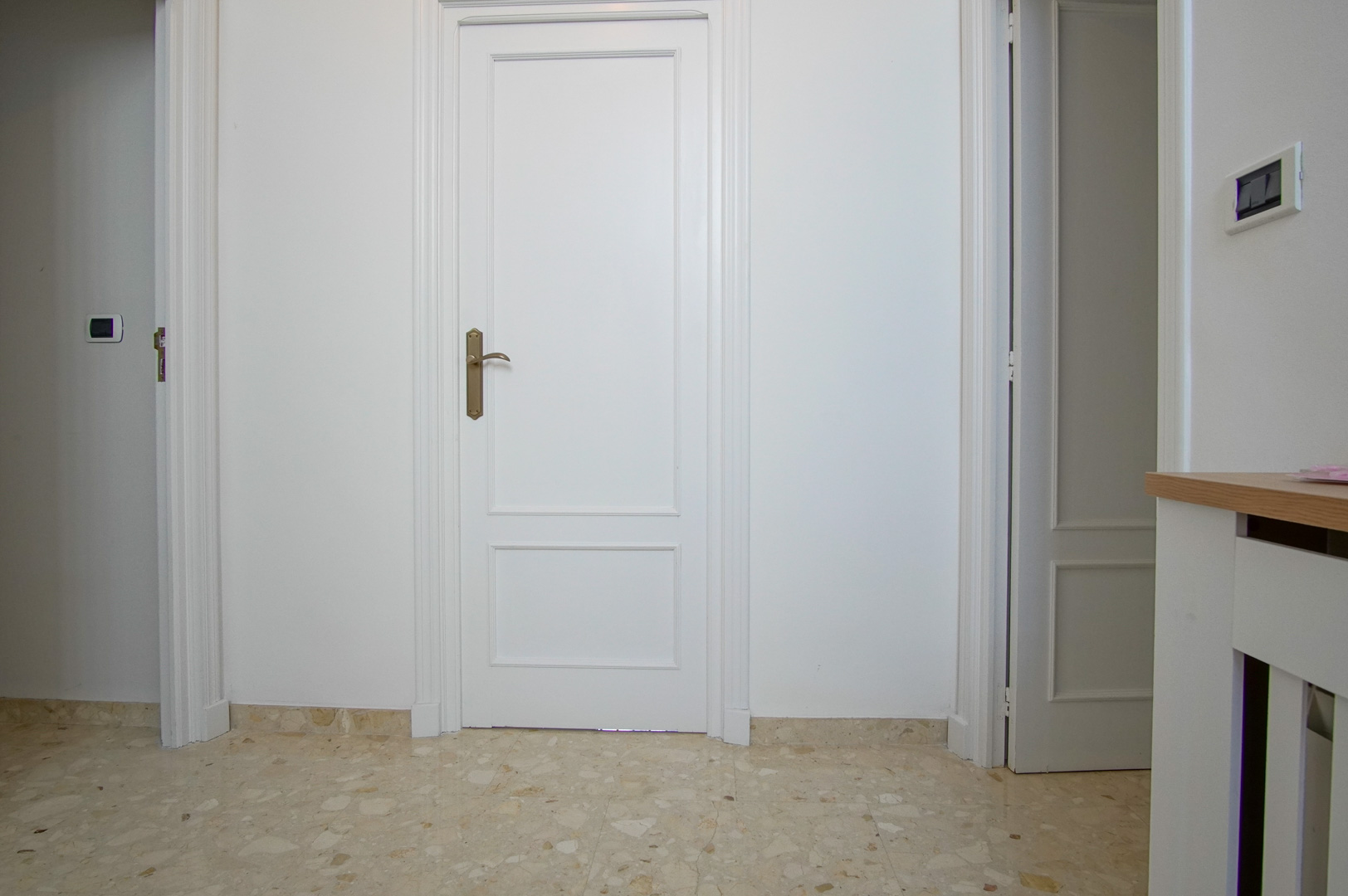 Interior hallway featuring white lacquered paneled doors and polished marble flooring. The space is finished with classic moldings and brass-toned hardware.