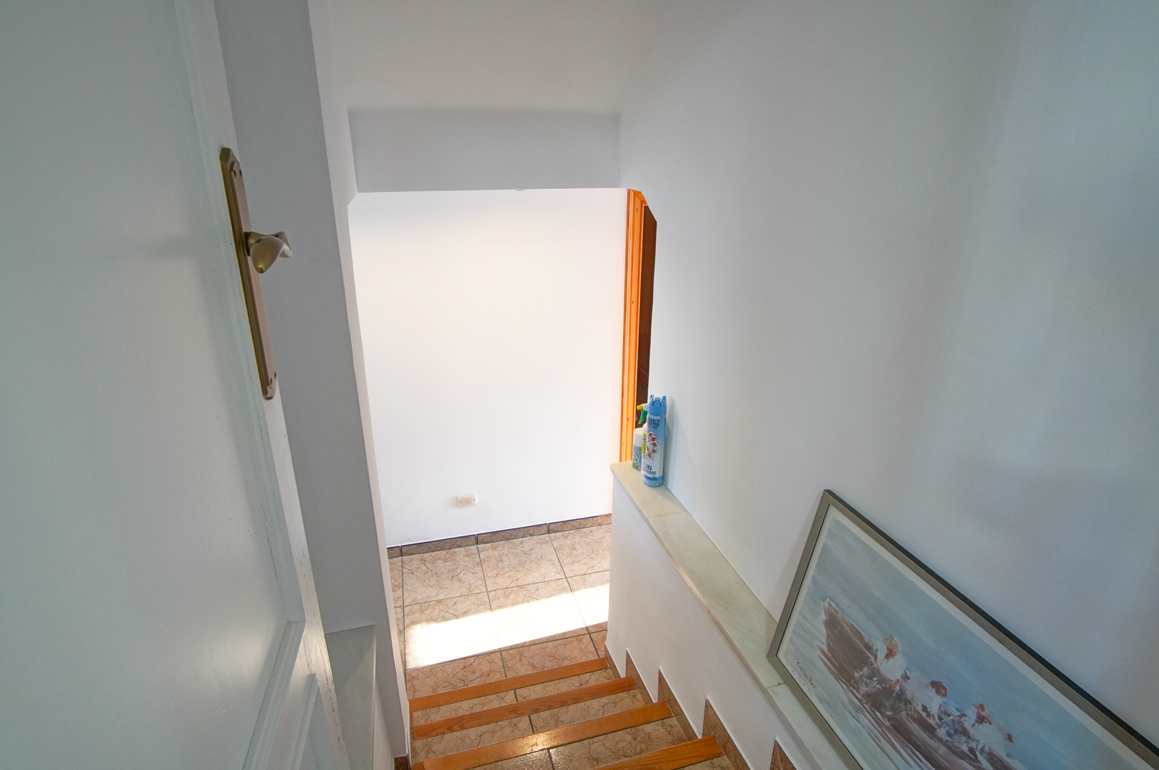 Interior staircase with wooden treads and ceramic tiling, connecting floors through a bright transition space with clean white walls.