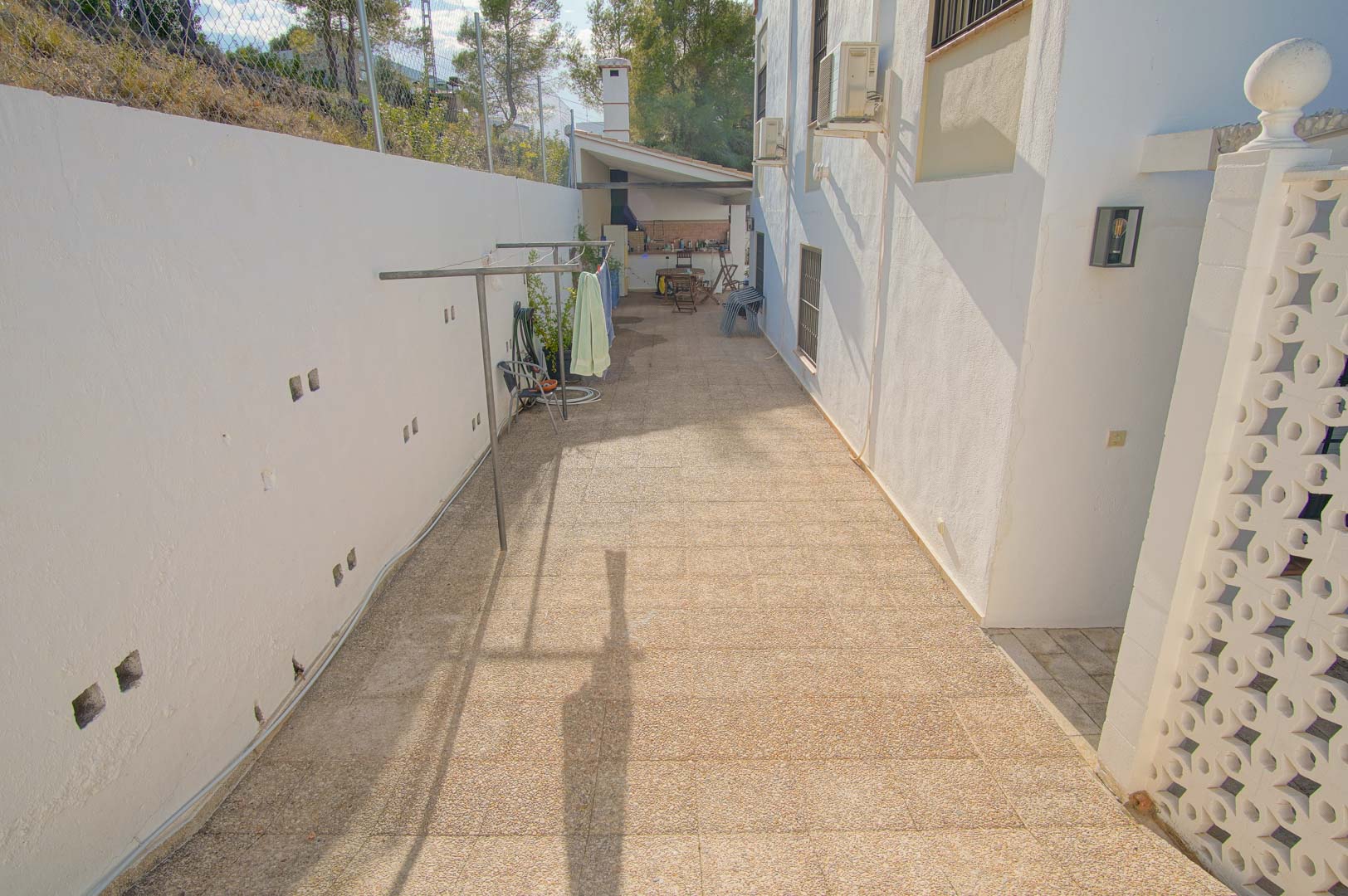 Paved side corridor featuring a utility area with a clothesline, leading toward the covered outdoor barbecue and kitchen.