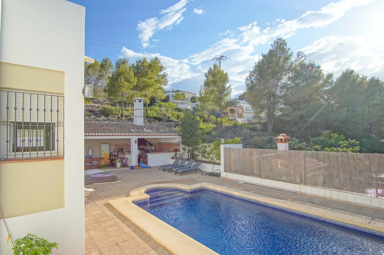 Private swimming pool featuring a spacious stone terrace, a covered outdoor kitchen with a chimney, and views of the lush Montgó hillside.