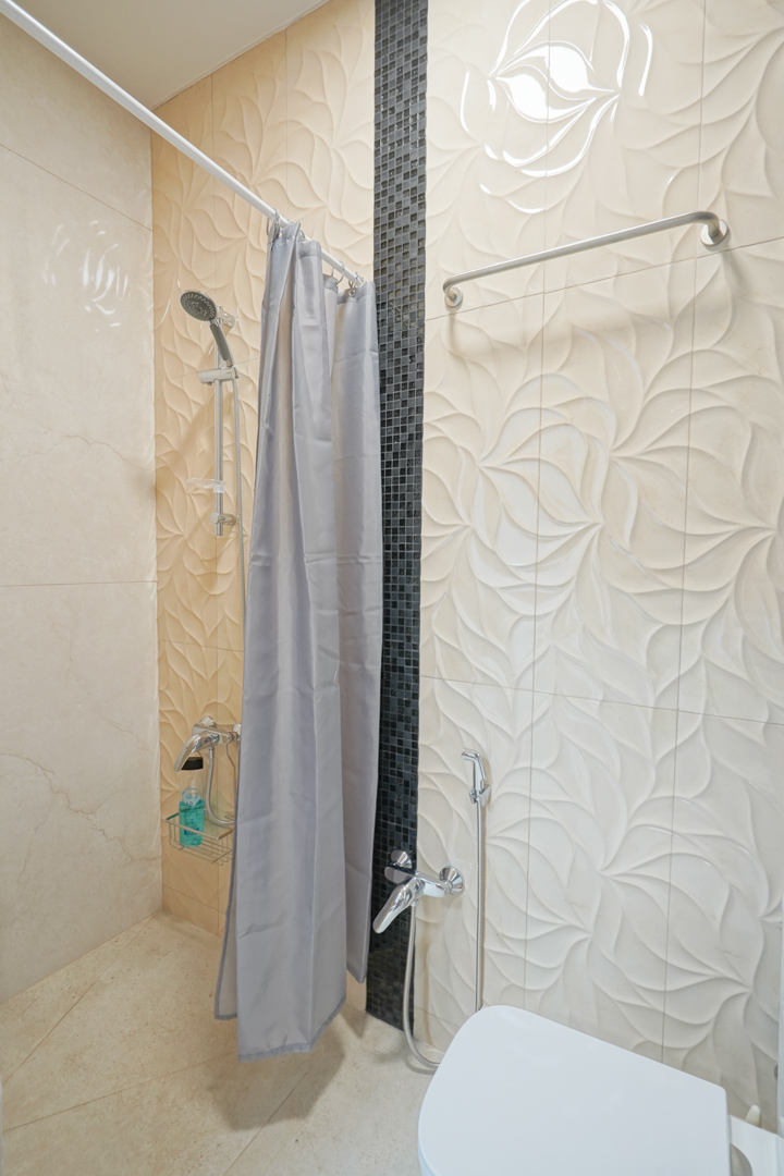Bathroom featuring cream floral relief wall tiles, a vertical black mosaic accent, and chrome fixtures including a handheld sprayer.
