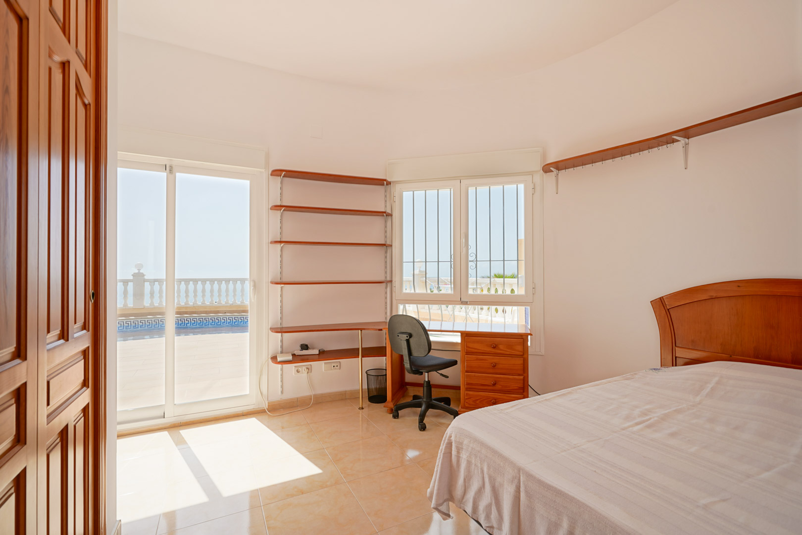 Bedroom featuring a wooden desk, wall shelving, and direct access to the terrace via sliding doors. Bright interior with ceramic tile flooring.