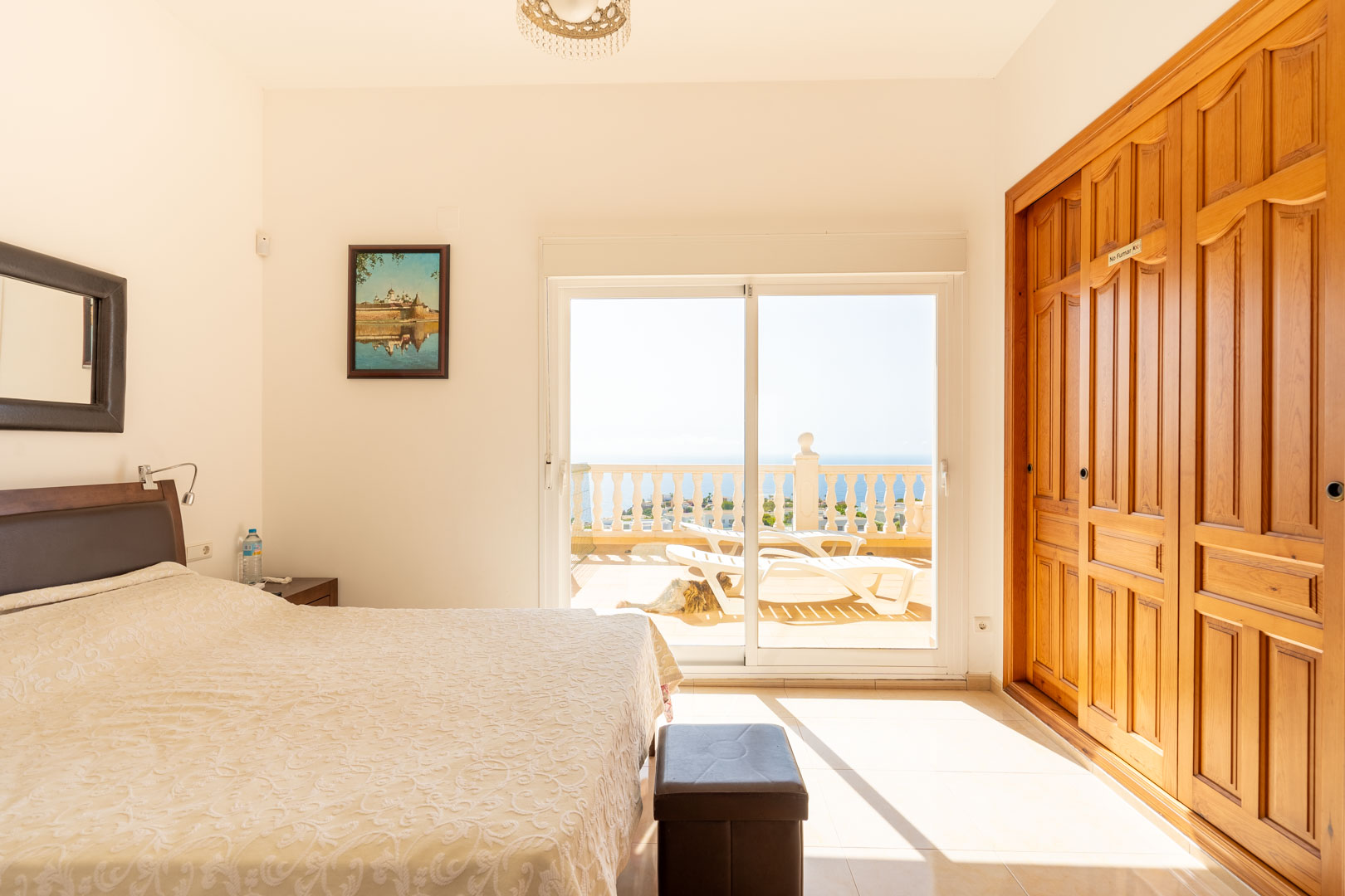 Bedroom featuring built-in wooden wardrobes and sliding glass doors that open onto a private terrace with sea views and sun loungers.