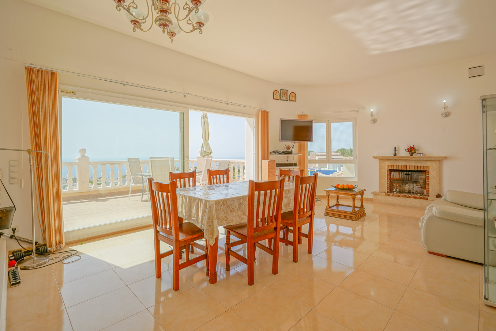 Bright living-dining area featuring a stone fireplace, ceramic flooring, and large sliding glass doors that open onto a terrace with Mediterranean sea views.