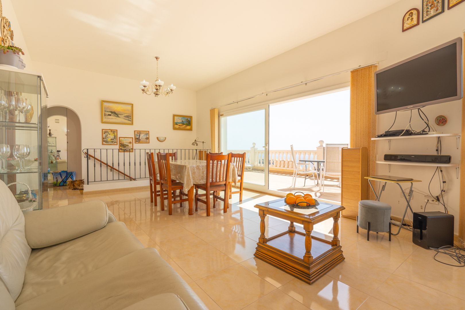 Bright living-dining room with polished tile flooring, featuring a wooden dining set and large sliding glass doors that open onto a sun-drenched terrace.
