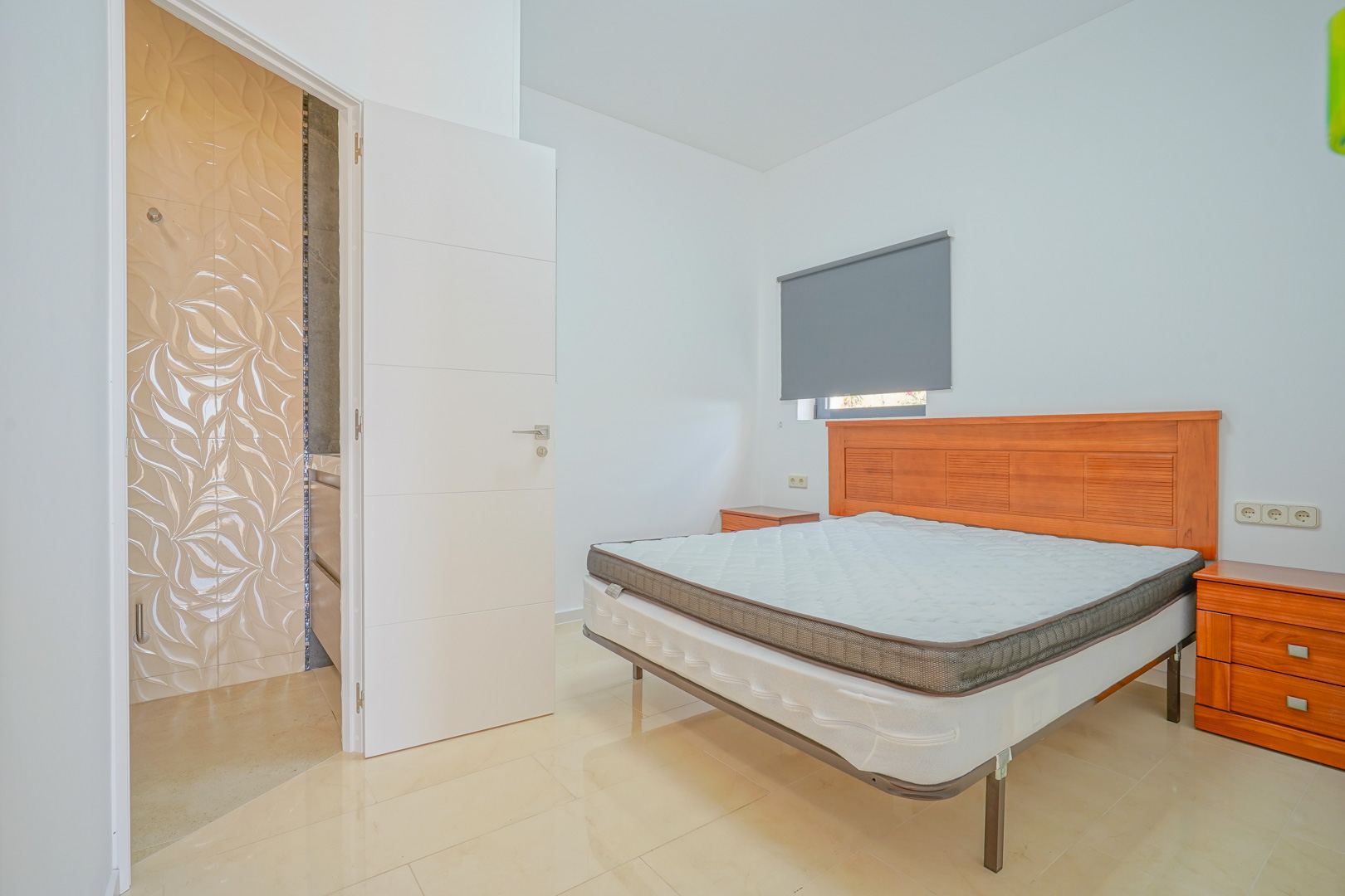 Double bedroom featuring wooden furniture, neutral tiled flooring, and an ensuite bathroom with distinctive textured wall tiles.