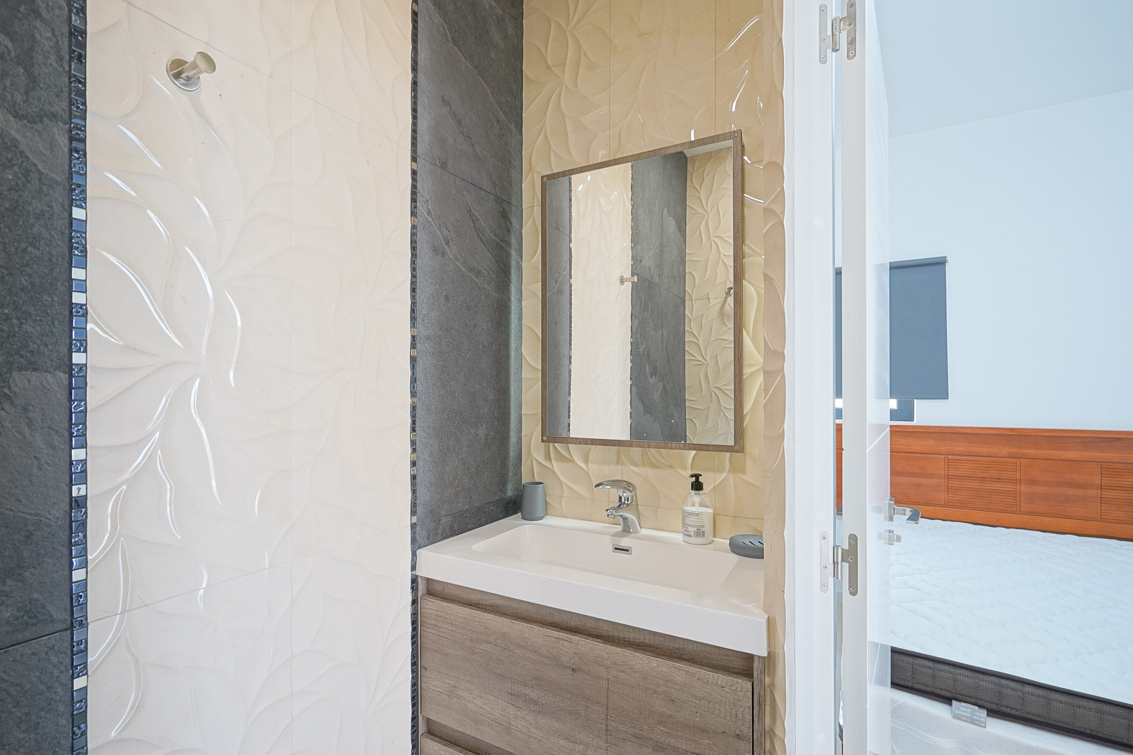 Ensuite bathroom featuring a wooden vanity, integrated white sink, and decorative textured wall tiles with dark slate accents.