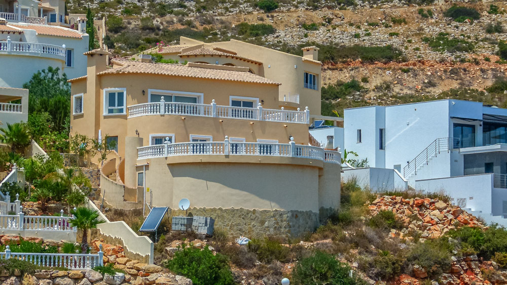 Exterior view of the Mediterranean-style villa featuring ochre facades and expansive curved terraces with white balustrades, built into the hillside.
