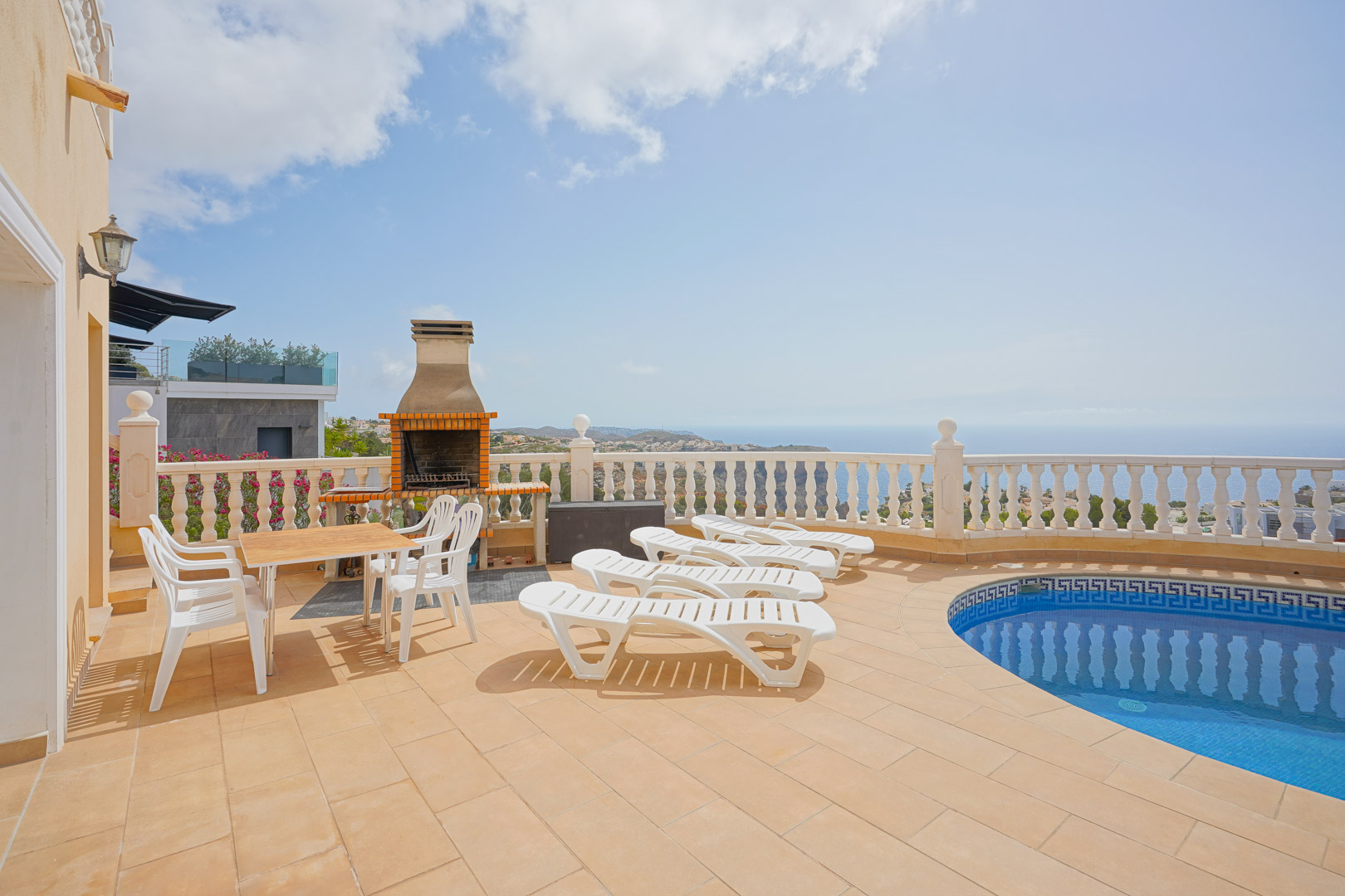 Outdoor terrace featuring a curved swimming pool, built-in brick barbecue, and sun loungers overlooking the Mediterranean Sea and coastal cliffs.