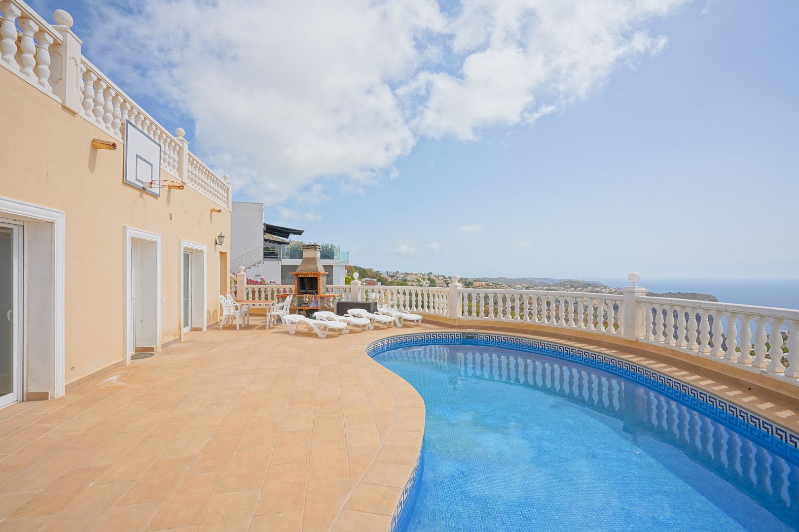 Outdoor terrace featuring a kidney-shaped pool with Greek key tiling, a built-in brick barbecue, and panoramic Mediterranean Sea views behind a white balustrade.
