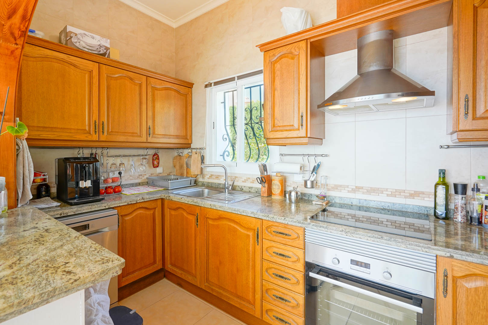 Semi-open kitchen featuring classic wood cabinetry, granite countertops, and stainless steel appliances, including an integrated oven and extractor hood.