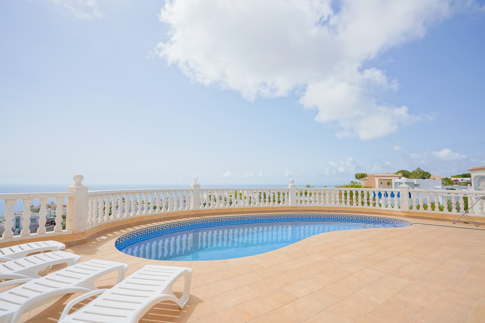 Terrace featuring a curved swimming pool with a Greek key border, white stone balustrade, and panoramic Mediterranean Sea views.