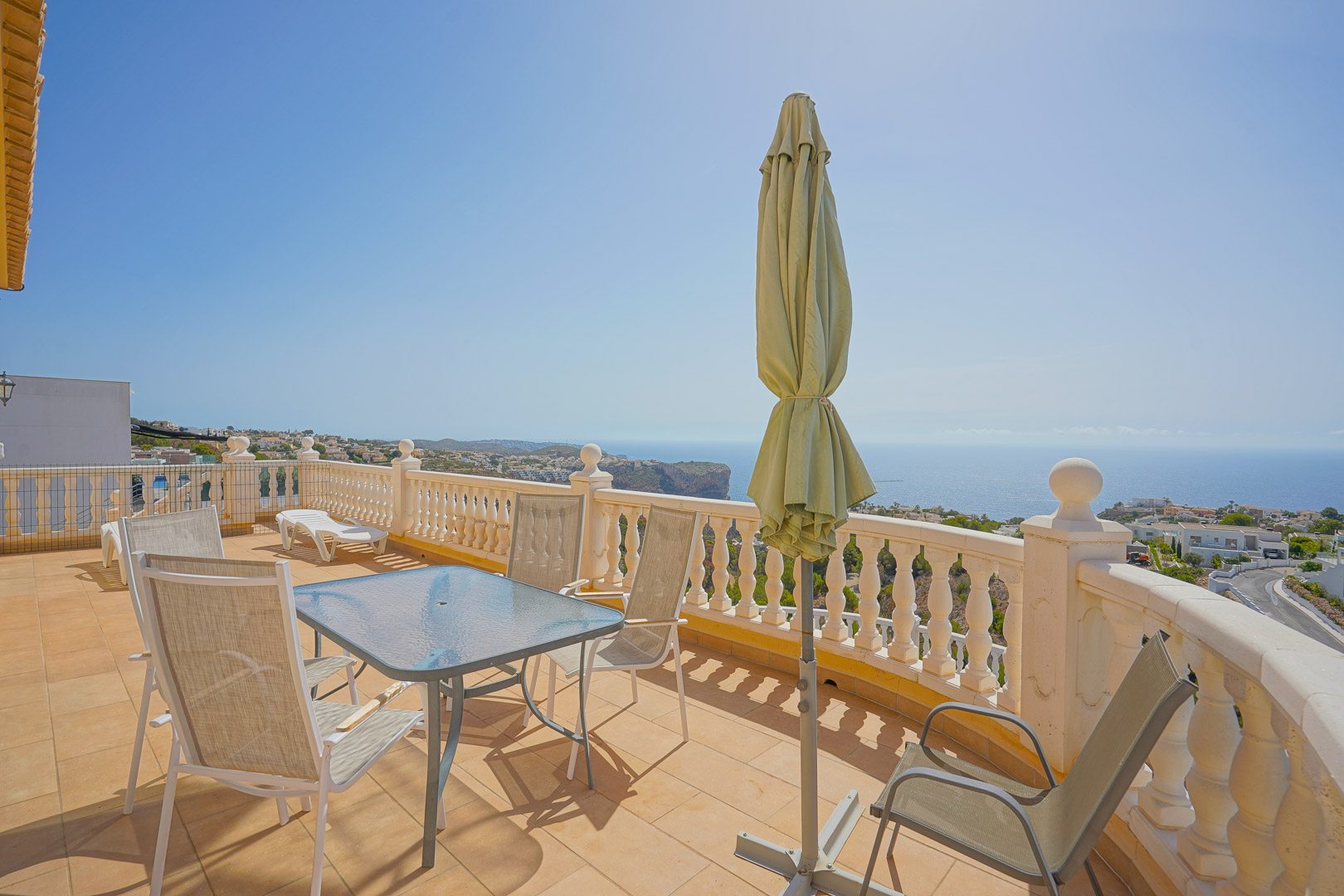 Upper terrace featuring a glass-top dining table, outdoor seating, and a white balustrade overlooking the Mediterranean Sea and coastal cliffs.