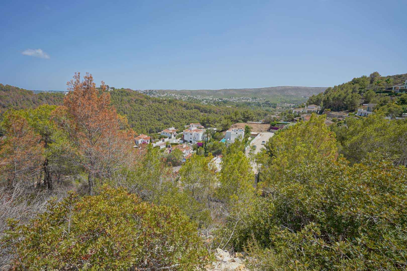 Elevated view from the plot overlooking the valley, featuring native Mediterranean vegetation and white villas nestled among the rolling green hills.