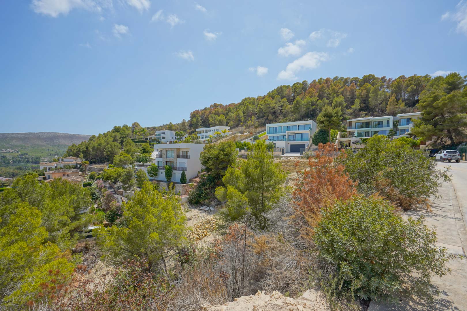 Elevated view of the residential area showing modern villas integrated into the natural slope, surrounded by native Mediterranean vegetation.