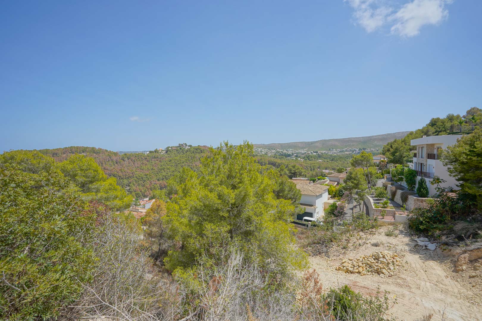Panoramic view from the elevated plot overlooking forested hills and modern villas integrated into the Mediterranean landscape.